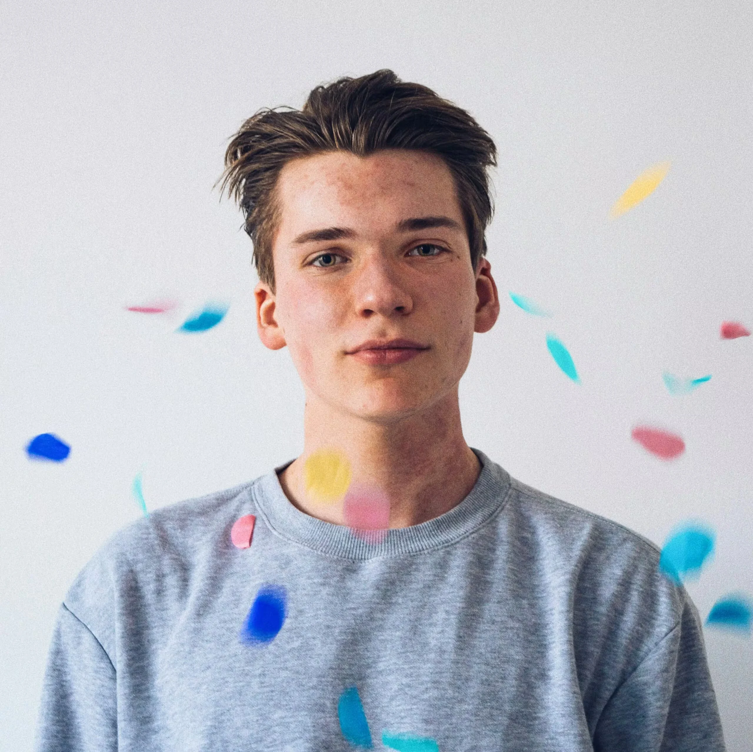 Young man in a gray shirt with colorful confetti falling around him.