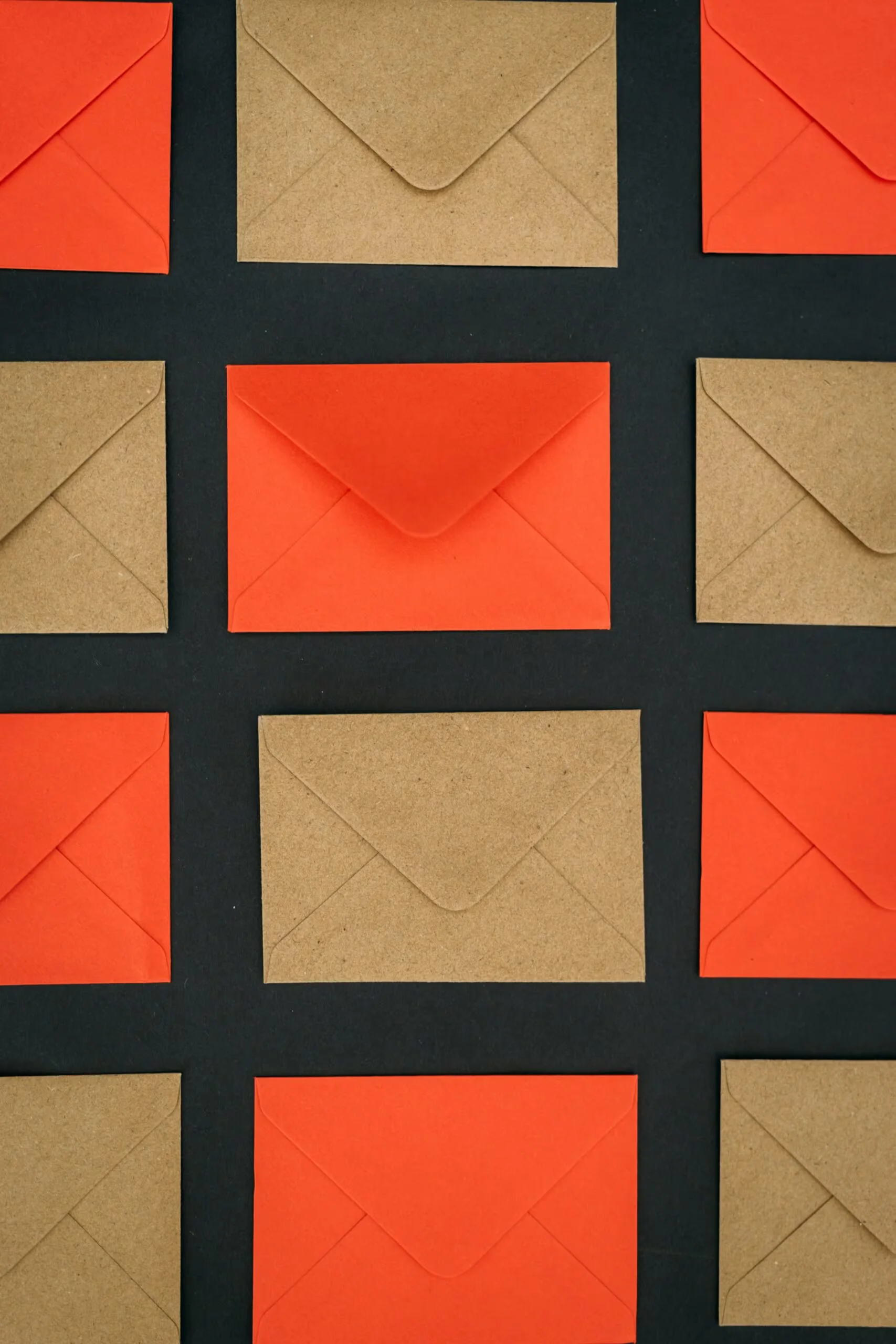 kelly-sikkema-80DgUsAayq4-unsplash • WaltosTech Grid of orange and kraft-brown envelopes laid out on a dark surface.
